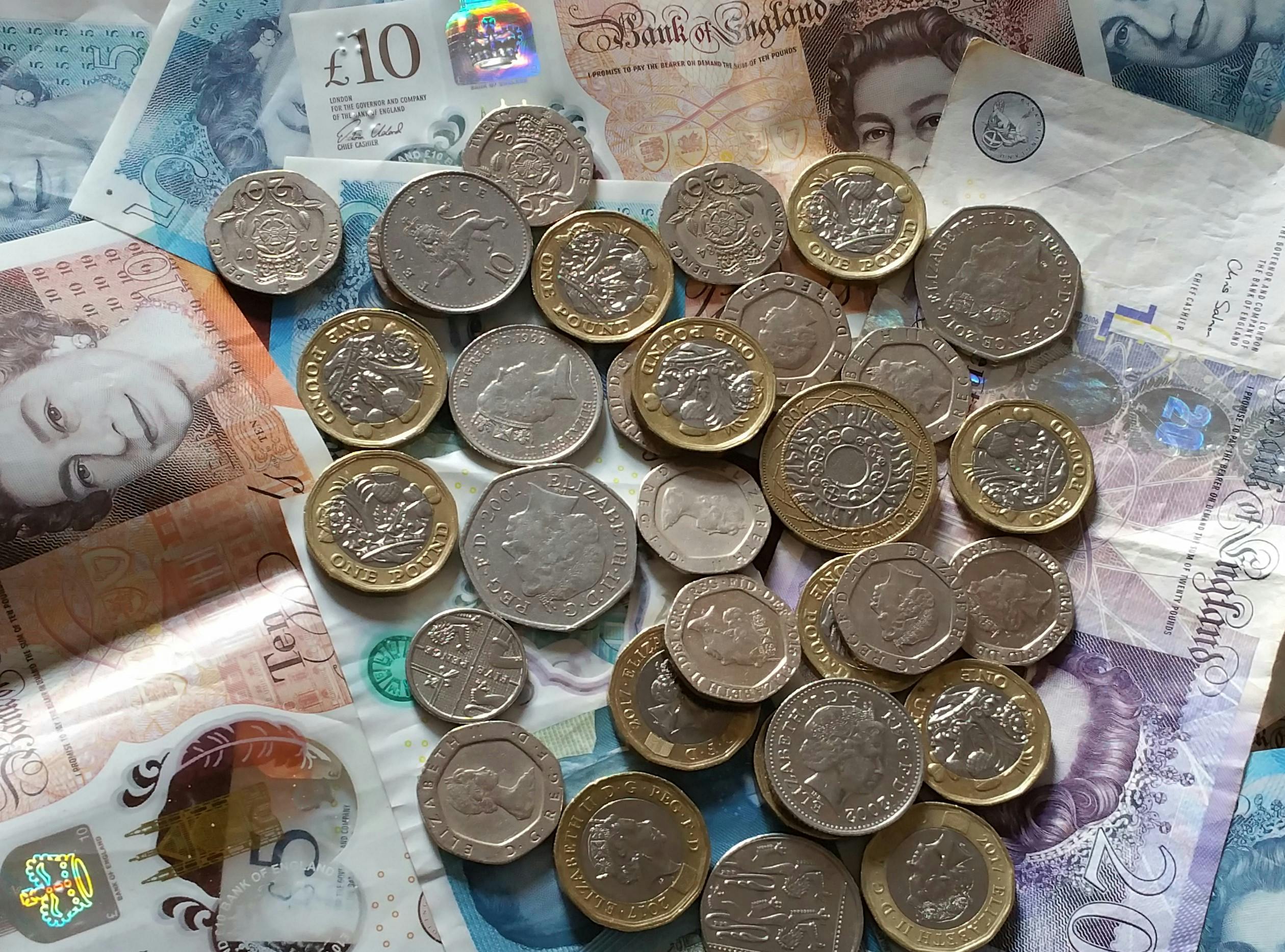 A pile of UK coins scattered across various British banknotes.