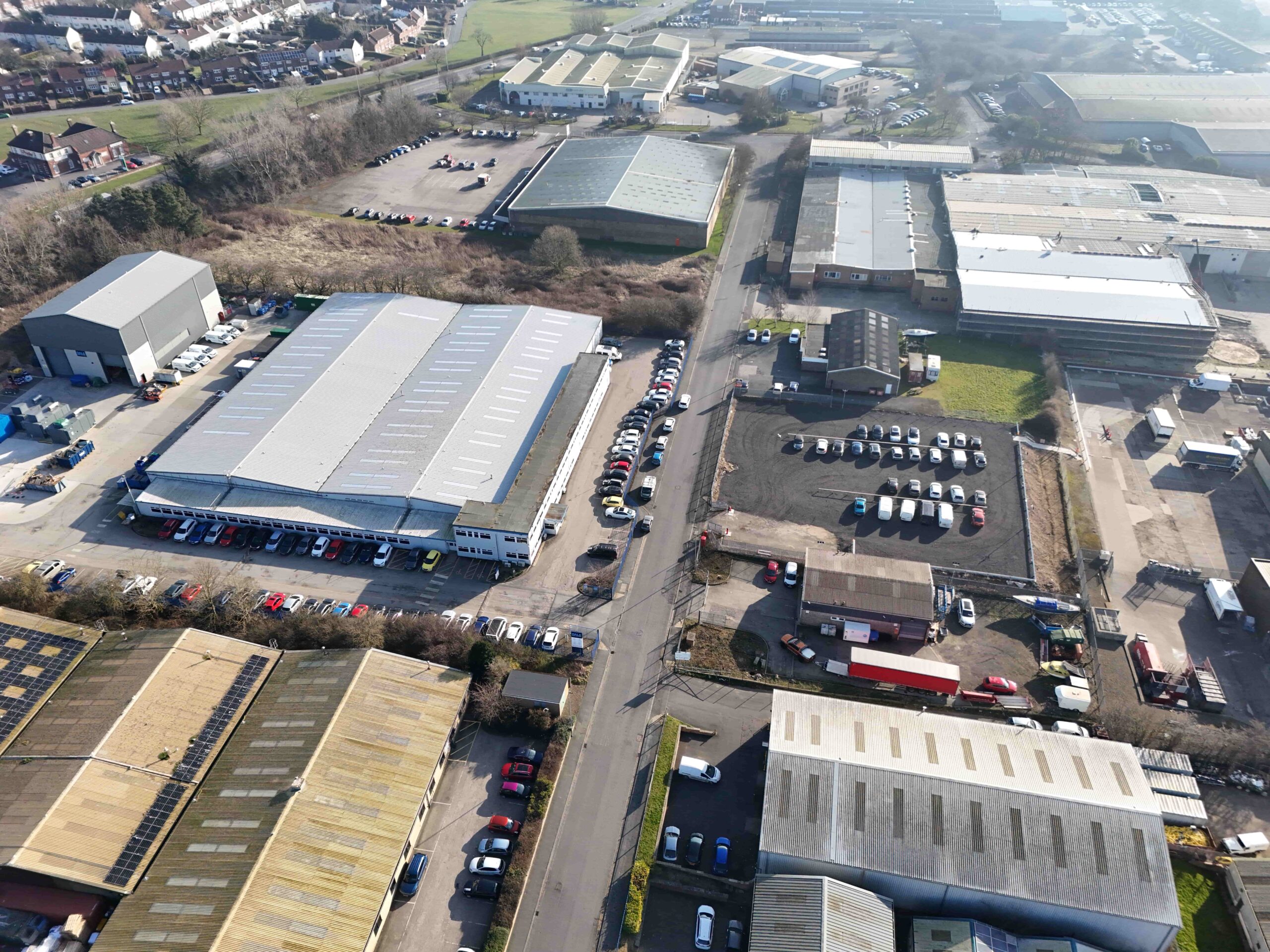 invest-strategic-Scarborough Business Park_D_14 (1) Aerial view of an industrial estate with several warehouse buildings, parking areas, and nearby residential areas in the background