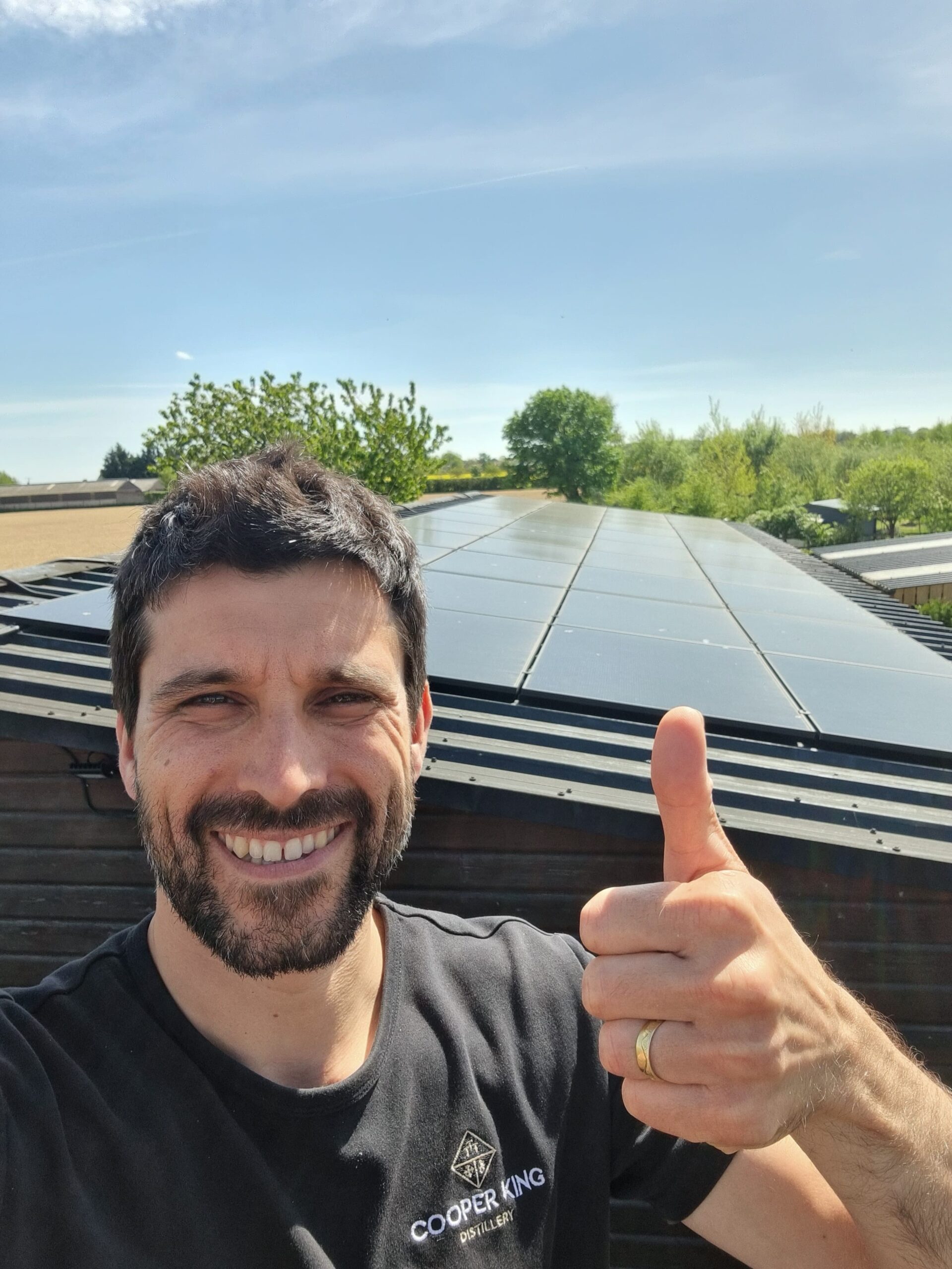 business-support-businesses-helped-cooper-king Person giving a thumbs-up in front of rooftop solar panels on a sunny day.